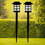 A pair of sleek black solar garden lights illuminating a lush green lawn at dusk.