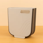 Collapsible hanging trash can mounted on a kitchen cabinet door, collecting food waste.