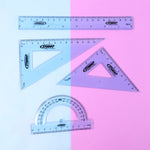 Transparent geometry tools laid out on surface showing ruler, protractor and set squares