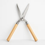 Angled view of the Indo Glow Hedge Shears, highlighting both the wooden handles and the sharp steel blades.