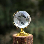 Elegant Crystal World Globe with golden stand, displayed next to a book and pen for desk decor.