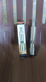Compact stainless steel thumb press salt and pepper grinder on a wooden surface.