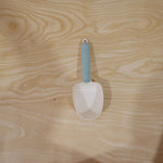 A white plastic measuring spoon demonstrating its use as a bag clip on a food bag.